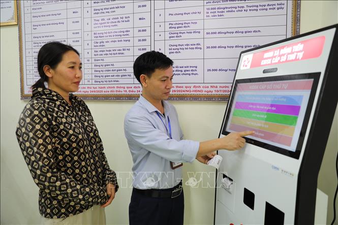 Cán bộ Trung tâm phục vụ hành chính công xã Đồng Tiến hướng dẫn người dân sử dụng máy lấy số thứ tự tự động. Ảnh: Khiếu Tư - TTXVN

