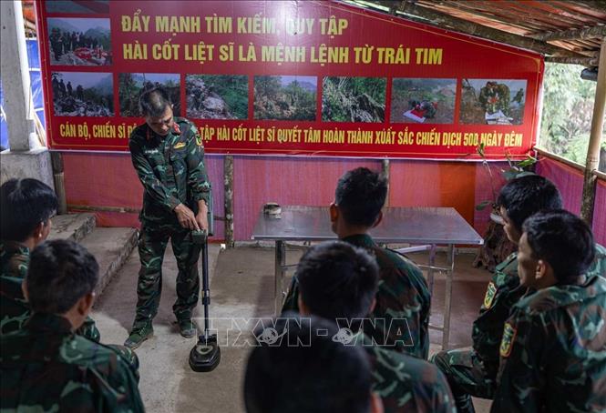 Thiếu tá quân nhân chuyên nghiệp Lê Văn Quyết hướng dẫn các thành viên trong Đội sử dụng máy dò mìn, đảm bảo an toàn khi tìm kiếm. Ảnh: Hoàng Hiếu - TTXVN