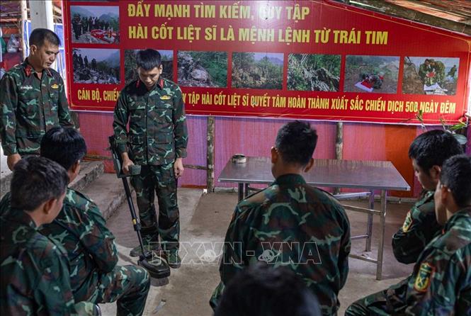 Thiếu tá quân nhân chuyên nghiệp Lê Văn Quyết hướng dẫn các thành viên trong Đội sử dụng máy dò mìn, đảm bảo an toàn khi tìm kiếm. Ảnh: Hoàng Hiếu - TTXVN