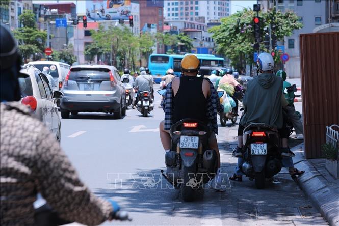 Người tham gia giao thông trên đường Tây Sơn dừng xe dưới râm tránh ánh nắng gay gắt trong lúc chờ đèn tín hiệu giao thông. Ảnh: Hoàng Hiếu - TTXVN