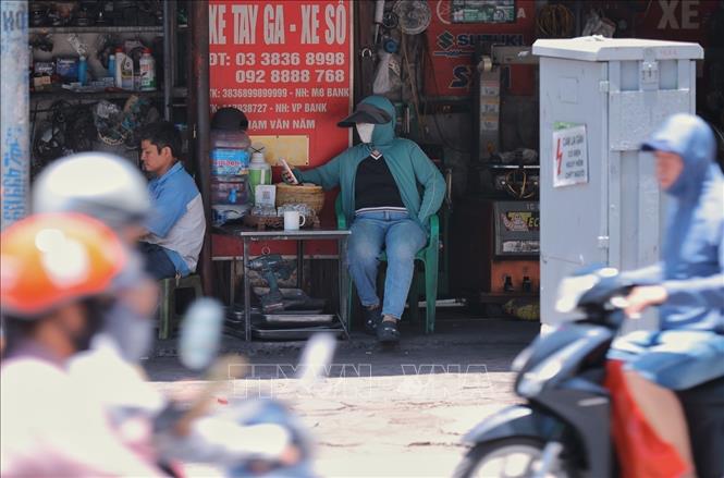 Dù ngồi trong bóng râm, người dân ven đường Võ Thị Sáu vẫn phải mặc đồ chống nắng do thời tiết oi bức. Ảnh: Hoàng Hiếu - TTXVN