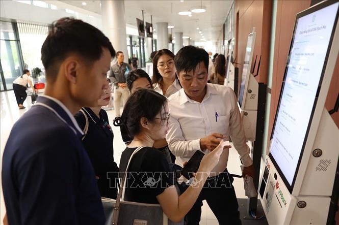 Cán bộ bệnh viên hướng dẫn người dân sử dụng máy lấy phiếu khám tự động. Ảnh: Tiến Long/TTXVN phát