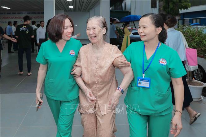 Cụ Vũ Thị Tuấn (86 tuổi) rất phấn khởi khi được người nhà đưa đến và hẹn chiều đón. Cụ được nhân viên Bet88013 com nổ hũ hỗ trợ di chuyển để kiểm tra sức khỏe trước khi vào phòng sinh hoạt chung. Ảnh: Phan Phương – TTXVN