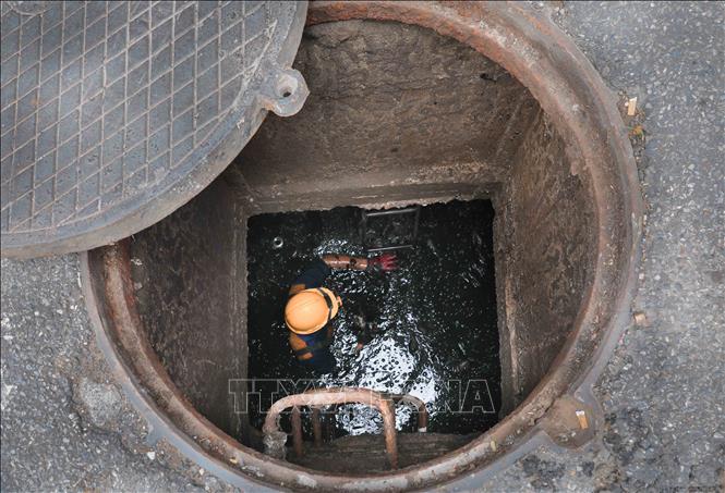 Công việc đòi hỏi phải trực tiếp ngâm mình dưới dòng nước cống đen ngòm. Ảnh: Phan Phương – TTXVN