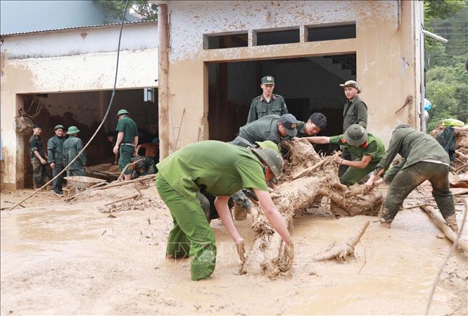 Lực lượng Công an giúp dân dọn bùn đất, đá, cây gỗ trôi vào nhà tại xã Mường Than. Ảnh: Quý Trung - TTXVN